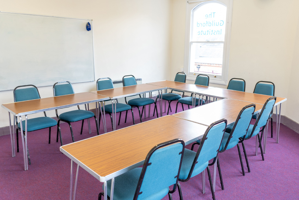 The Conference Room: view of a horseshoe table layout with 12 blue chairs. There is a large whiteboard mounted on the wall behind.