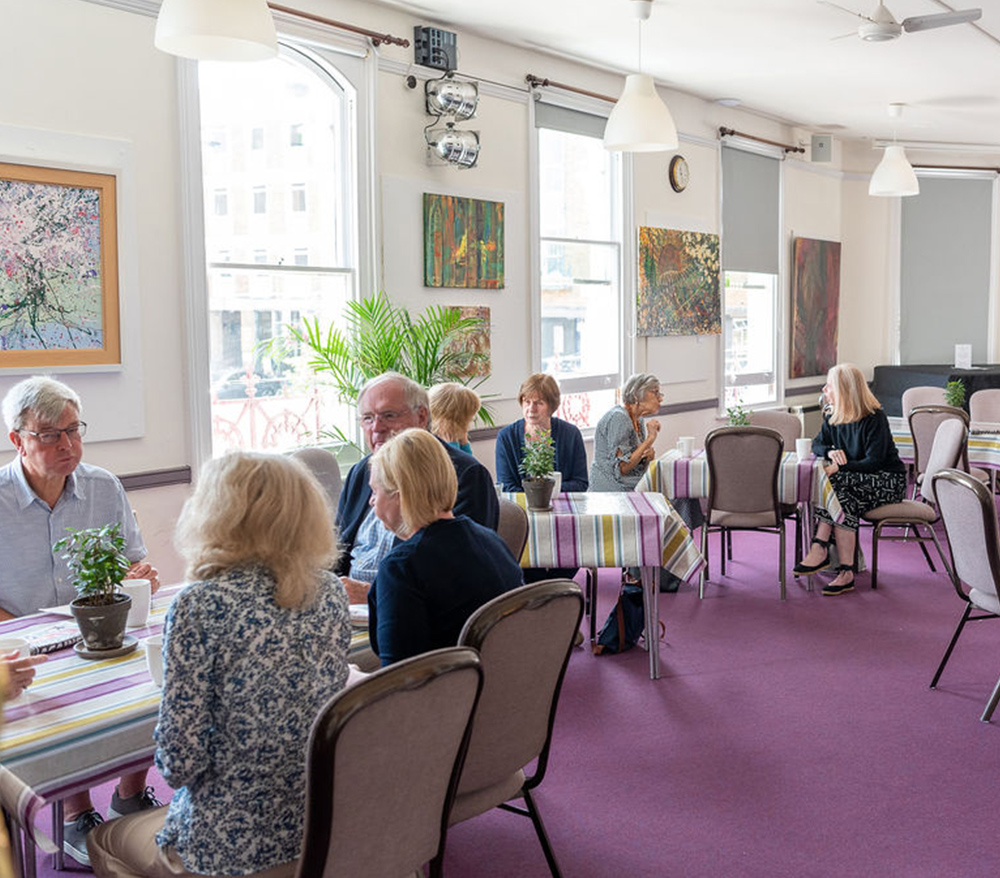 Groups of people sat at tables in V Café, chatting and drinking coffee.