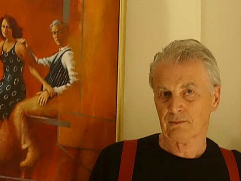 Ronnie Ireland, wearing a black t-shirt, standing in front of his painting which depict a man and a woman.