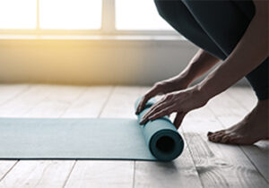 Figure crouched down onto the floor rolling out their yoga mat.