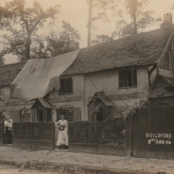 A black and white image of a mother and child stood outside a row of houses. Part of the roof is covered with a tarpaulin.