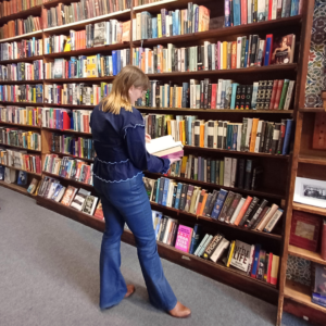 Woman stood in front of floor-to-ceiling bookshelves in library reading a book.