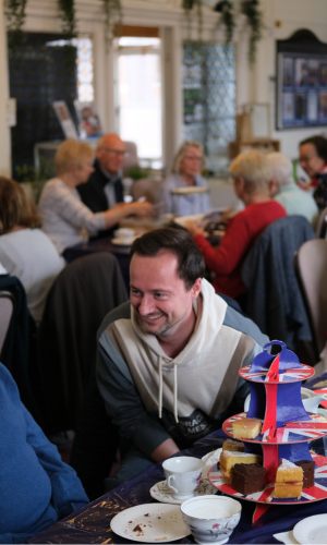 Man with dark brown hair, wearing a hoodie, sat smiling