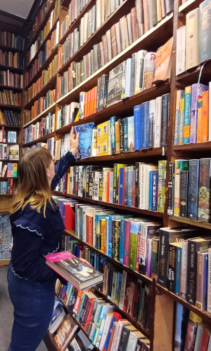Woman stood next to a floor-to-ceiling bookshelf, holding books
