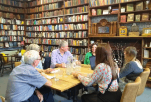 Six peopl sat around a table having a meeting in a library with floor-to-ceiling bookshelves